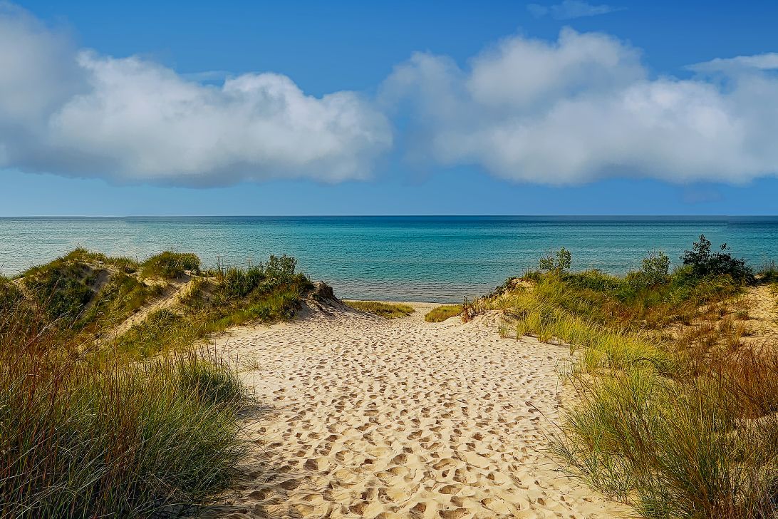 Northwest Indiana residents enjoy images at Indiana Dunes National Park like in this picture showing a sandy path down to the crystal blue waters of Lake Michigan against a sunny blue sky with clouds