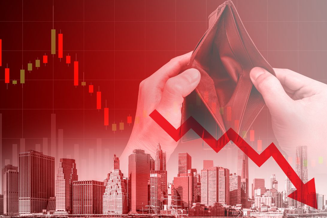 A red arrow pointing down with buildings and an empty wallet in the background to illustrate what is a recession