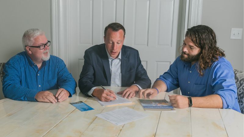 Three men in blue shirts at a conference table. These men are real estate agents Chuck Vander Stelt, David Spaliaras, and Karl Holleworth all members of the Quadwalls Real Estate Team at Listing Leaders. 